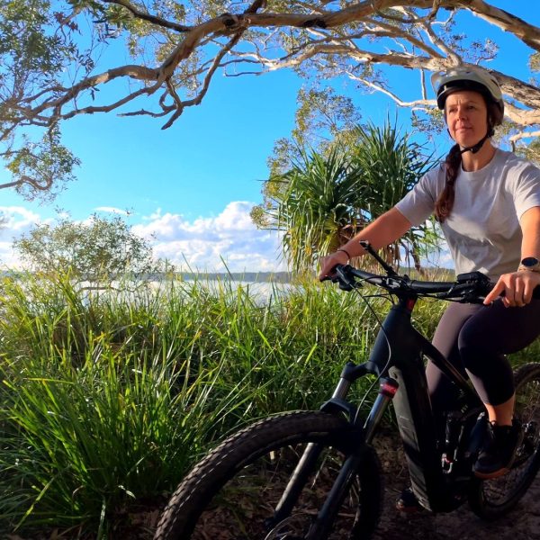 Smiling rider on a lakeside mountain bike trail among pandanus, Noosa Hinterland