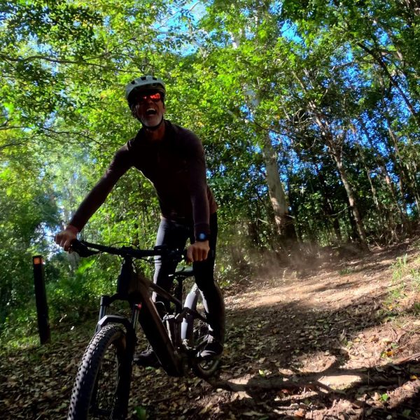 Smiling rider climbing forest singletrack on an e-mountain bike, Noosa