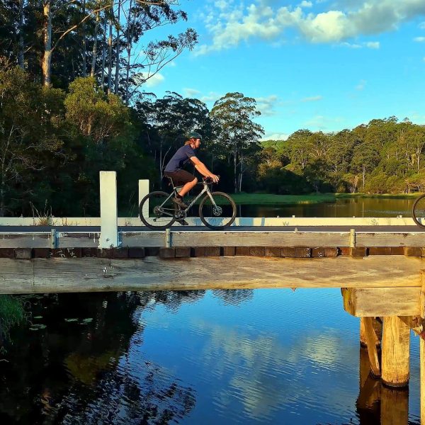 Riders crossing a timber bridge at golden hour, Noosa Hinterland multi-day bike journey